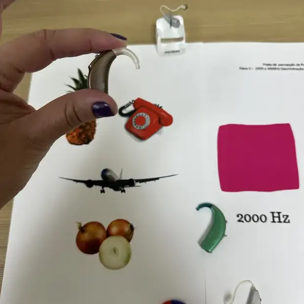 Mão segurando um aparelho auditivo retroauricular sobre a folha de figuras da atividade