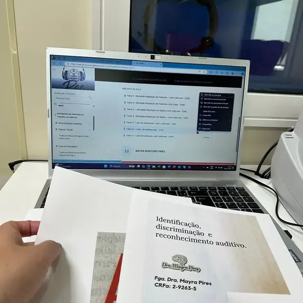 Notebook com a atividade aberta e o material impresso do PAC Memo na bancada do consultório