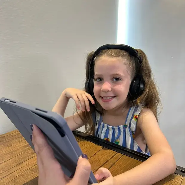 Criança com fones de ouvido fazendo uma atividade do PAC Memo no tablet