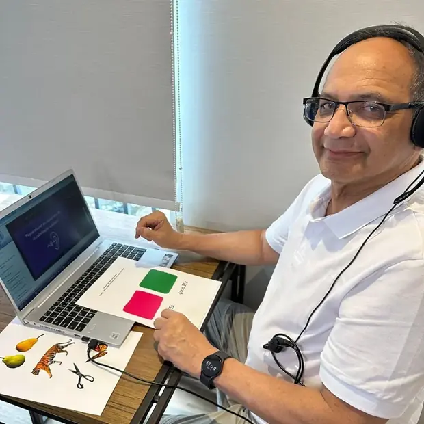 Homem idoso com fones de ouvido diante do notebook e das figuras coloridas da atividade